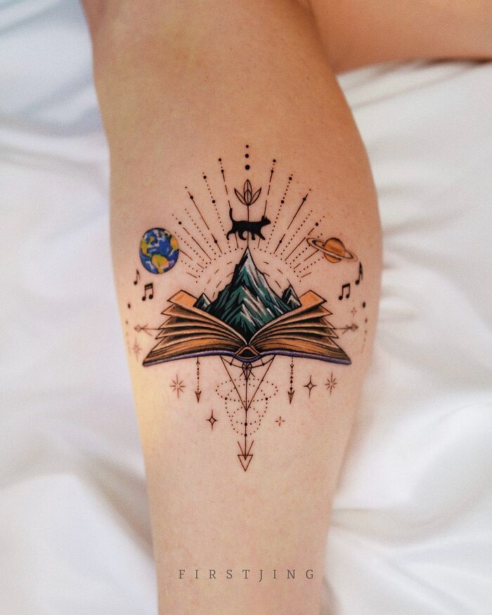 Fine-line tattoo featuring a book, mountains, planets, and animal in dreamy setting on leg.