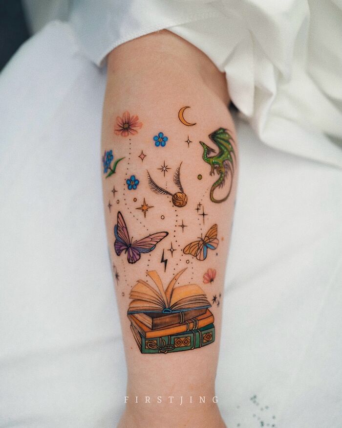 Colorful fine-line tattoo featuring books, butterflies, and a dragon in a dreamy setting on an arm.