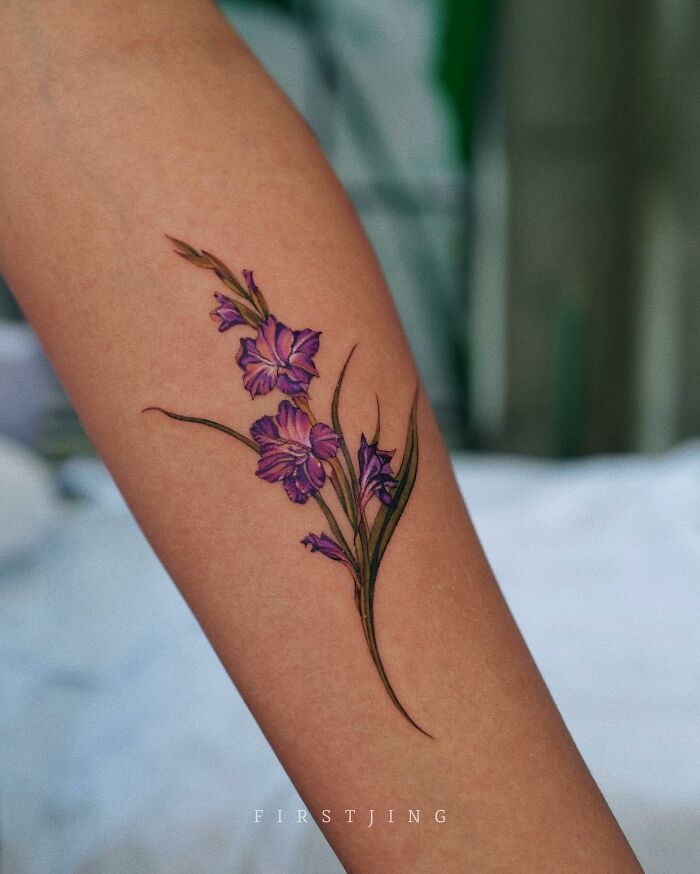 Fine-line tattoo of purple flowers on forearm, showcasing dreamy design.