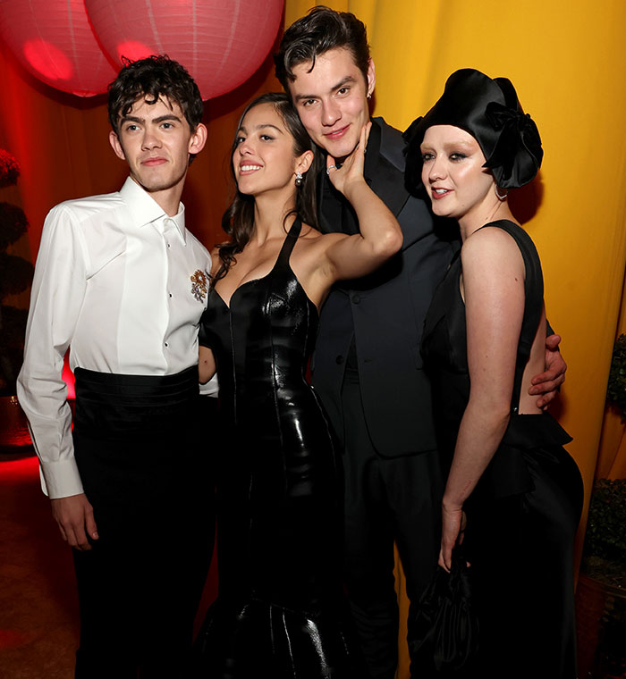Actors in formal attire at a behind-the-scenes moment during Oscars 2025, posing under red lantern lighting.