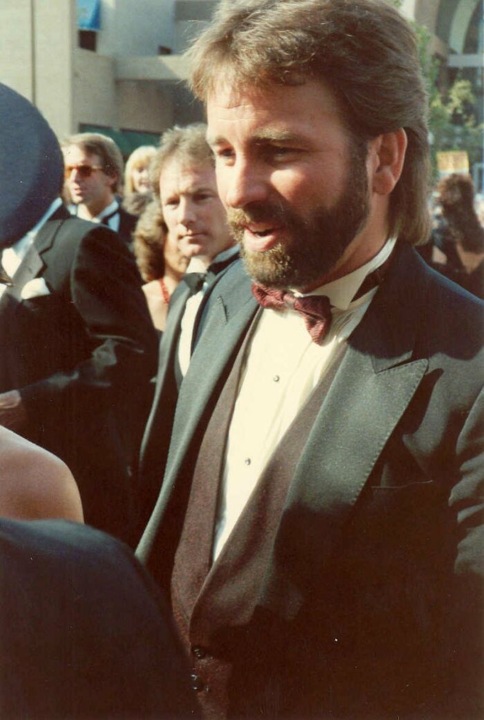 A man in a suit with a bow tie interacting with fans at a public event.