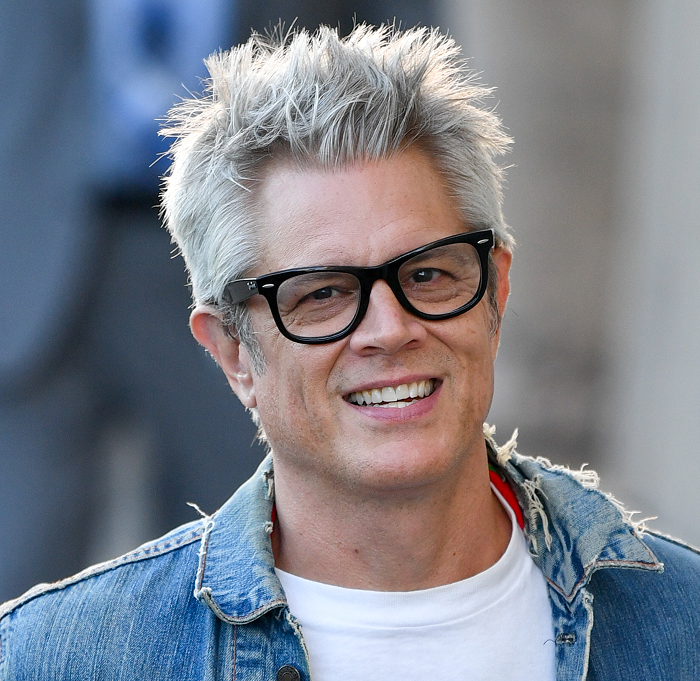 Man with gray hair and glasses in a denim jacket, smiling in a candid shot, embodying attractive celebrity style.