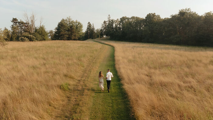 A couple walking hand in hand down a grassy path amidst a field, featured in top engagement photos of 2025.