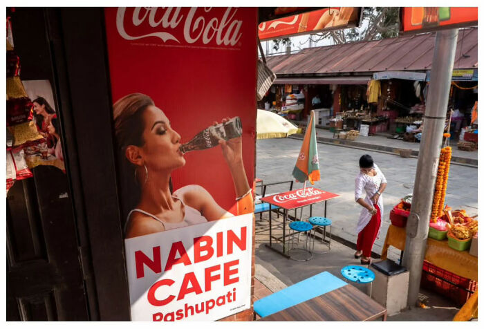 Street scene by Andrés Ramos featuring a cafe sign and market stalls, capturing unfiltered urban life moments.