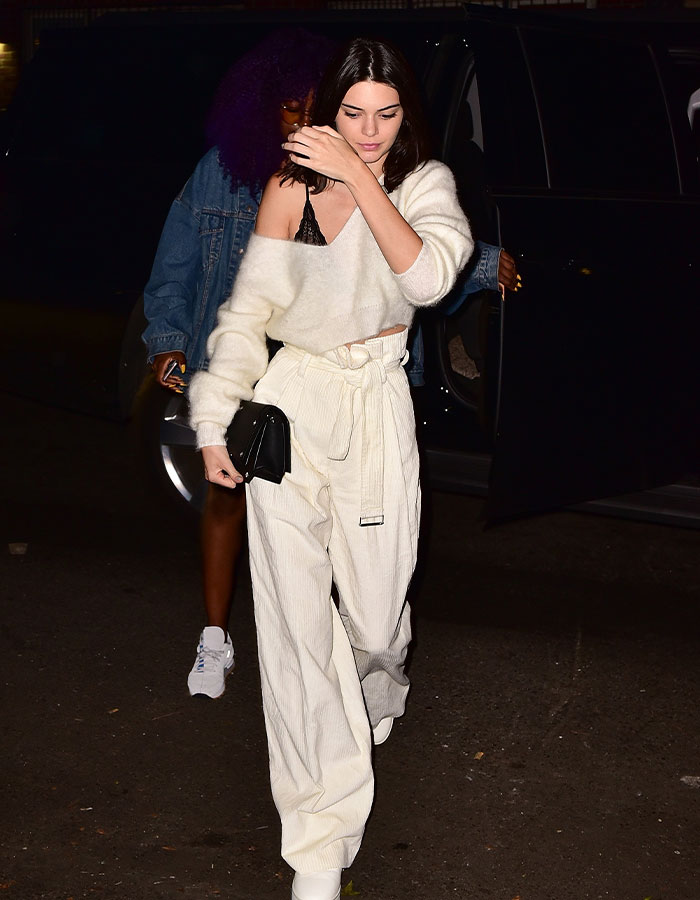 Celebrity wearing stylish budget-friendly outfit: white top, high-waisted pants, and a black clutch at night event.