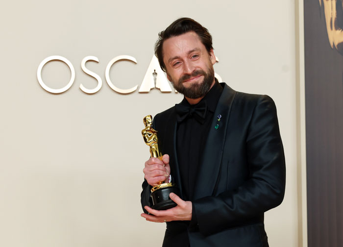 Man in a black suit holding an Oscar trophy, smiling at the Oscars 2025 event.