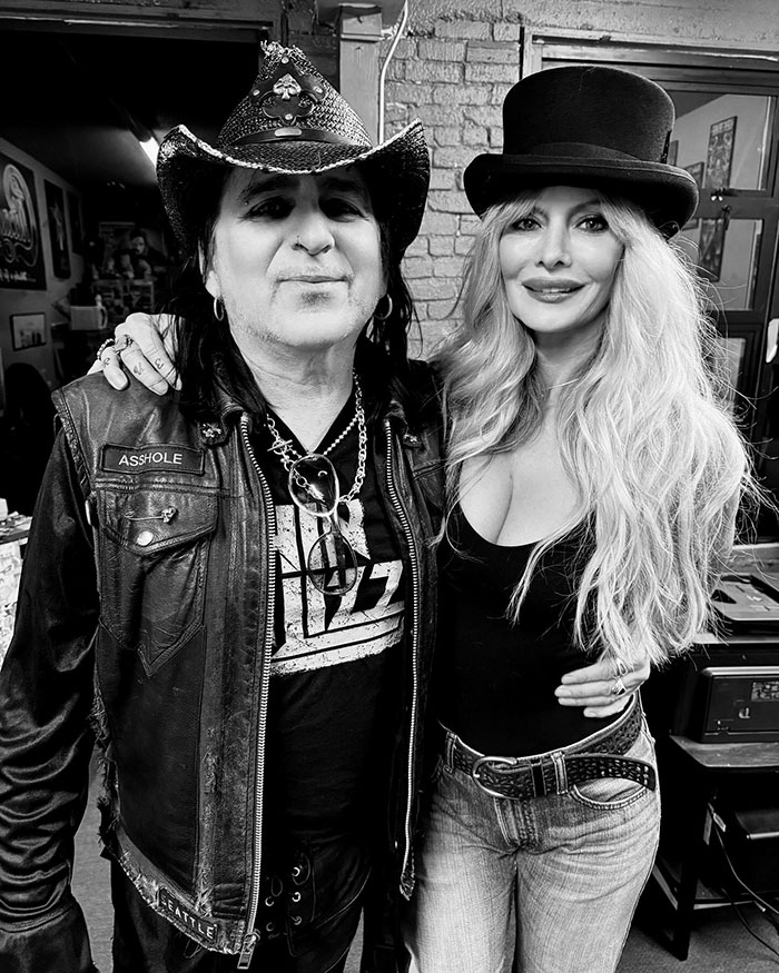 Man and woman posing together, both wearing hats, embodying glam metal style. Man and woman posing together, both wearing hats, embodying glam metal style.