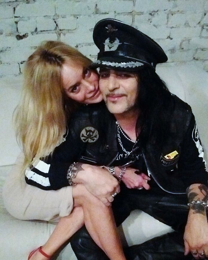 A couple sitting together on a couch, the man wearing a decorated hat and leather jacket; concept of a toxic relationship. A couple sitting together on a couch, the man wearing a decorated hat and leather jacket; concept of a toxic relationship.