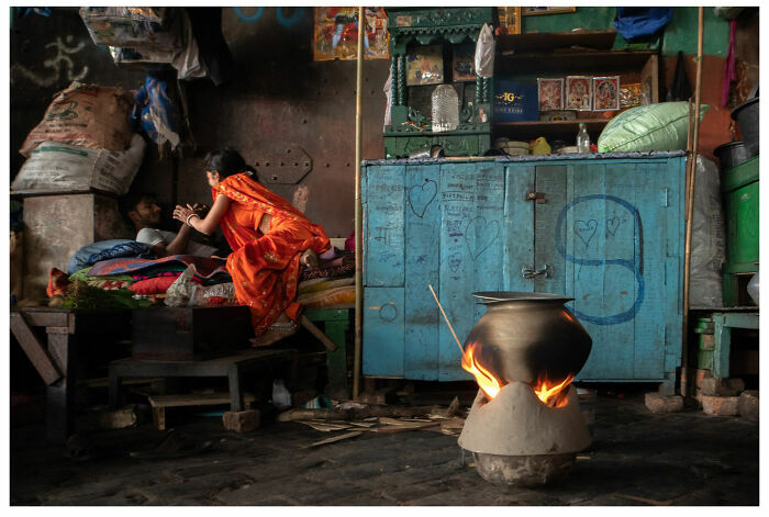 A woman in a vibrant sari chats with a man in a colorful street corner, with a pot boiling nearby.