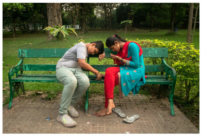 Two people sit closely on a park bench, deeply focused on their smartphones, capturing a raw street moment.
