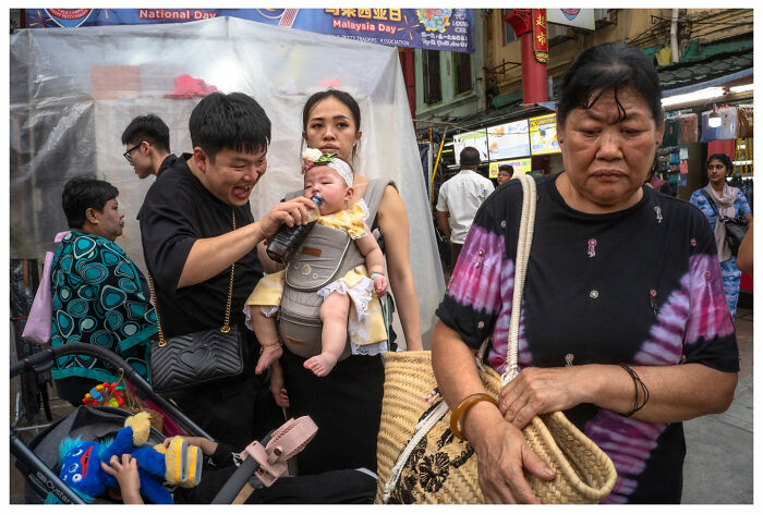 Street scene by Andrés Ramos showing diverse people, including a family with a baby, capturing candid unfiltered moments.
