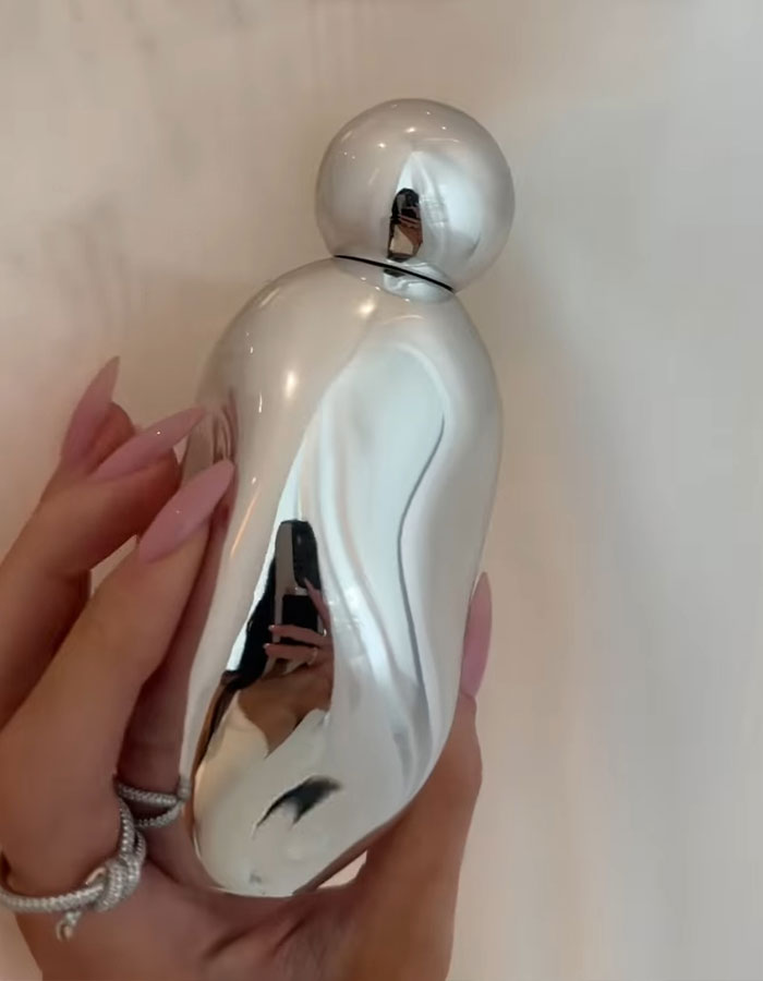 A person holding a shiny perfume bottle with a unique, curvy shape.