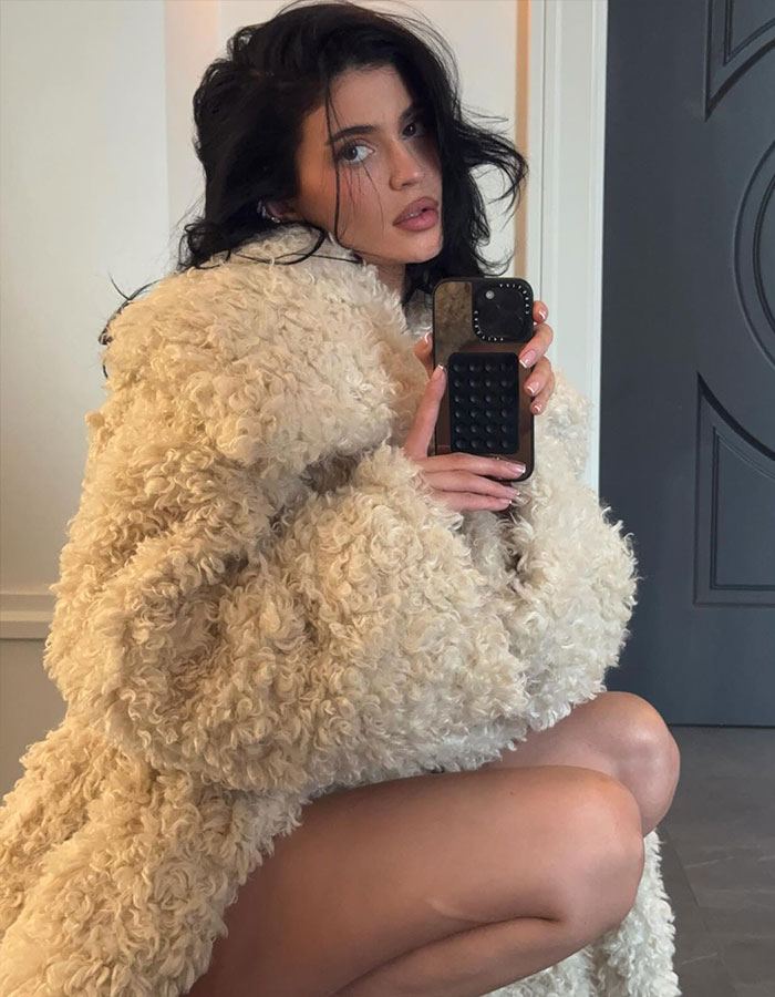 Woman in a fluffy coat taking a mirror selfie, related to Kylie Jenner's new perfume bottle debate.