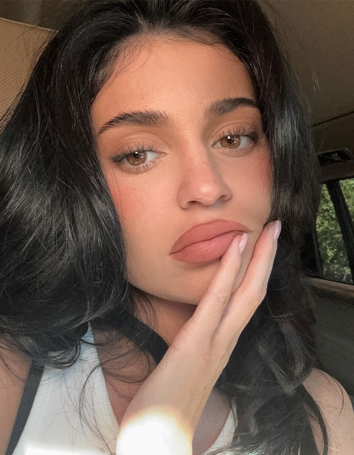 A woman with dark hair resting her chin on her hand, related to Kylie Jenner's new perfume bottle shape controversy.