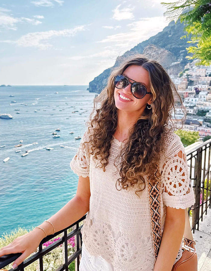 Smiling woman in sunglasses with curly hair enjoying a coastal view, representing a viral Georgia sorority girl story. Smiling woman in sunglasses with curly hair enjoying a coastal view, representing a viral Georgia sorority girl story.
