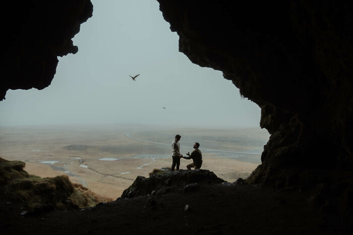 A couple in a cave, one kneeling to propose, with a vast landscape in view, part of the best engagement photos of 2025.