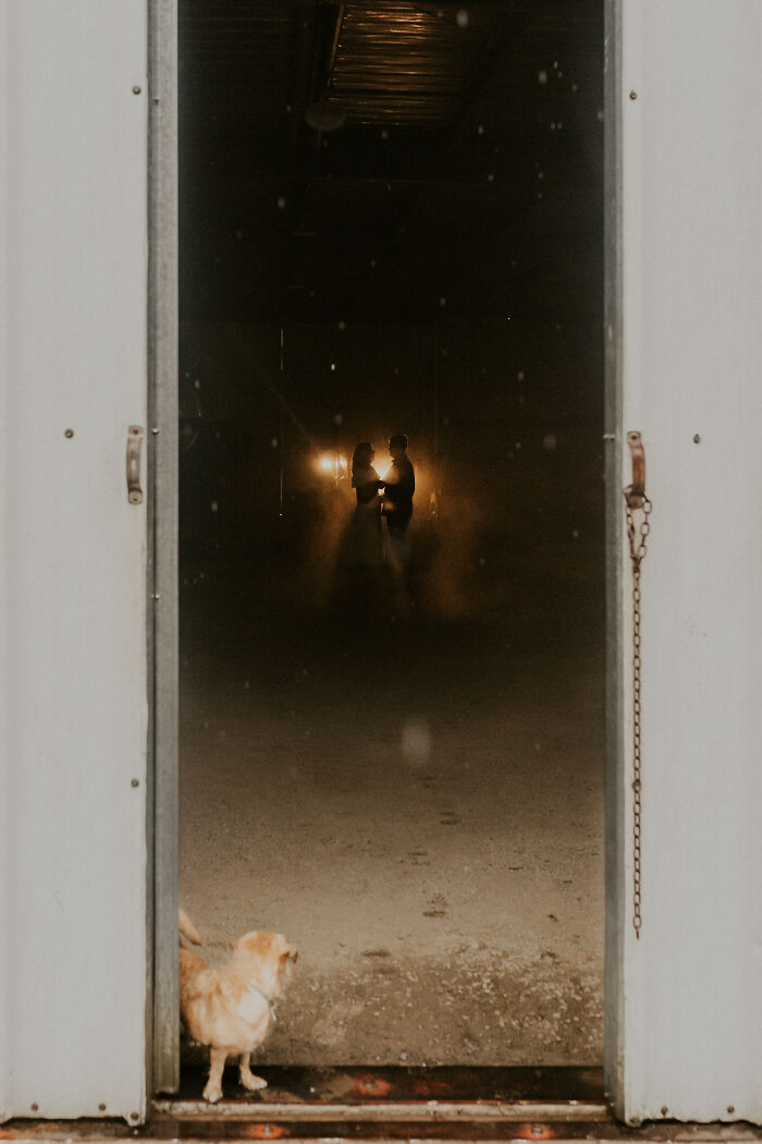 Couple holding hands in a dimly lit room, framed by an open door, capturing a top 2025 engagement photo.