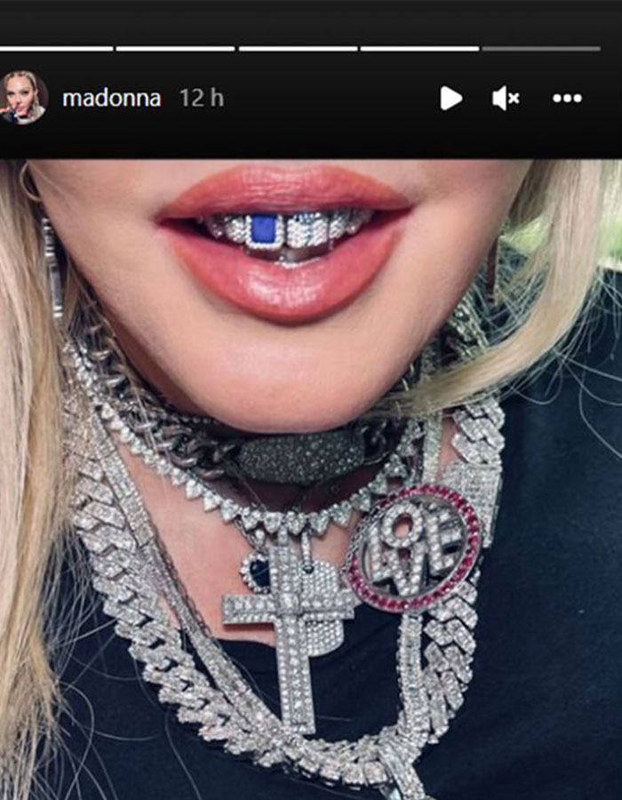 Dazzling diamond grills and necklaces with intricate designs worn by a smiling person.