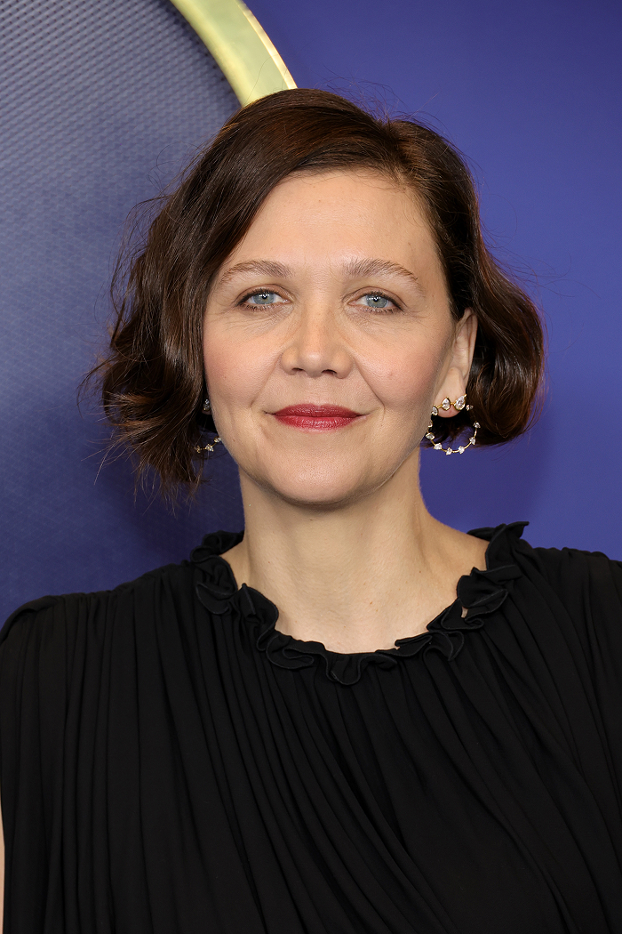 Celebrity with short hair and earrings, wearing a black dress, smiling at an event.