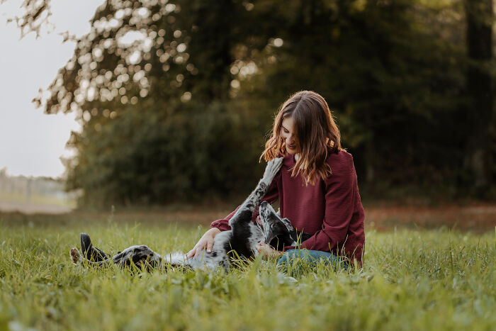 A woman in a maroon sweater sits in a grassy field, creating a special bond with her dog as they play together.