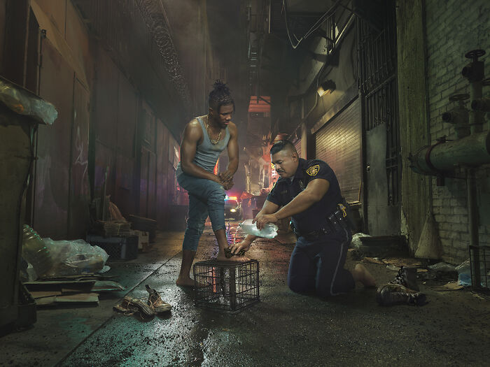 Police officer bandaging a man's foot in a dimly lit alley, part of the 2024 IPA stunning photos collection.