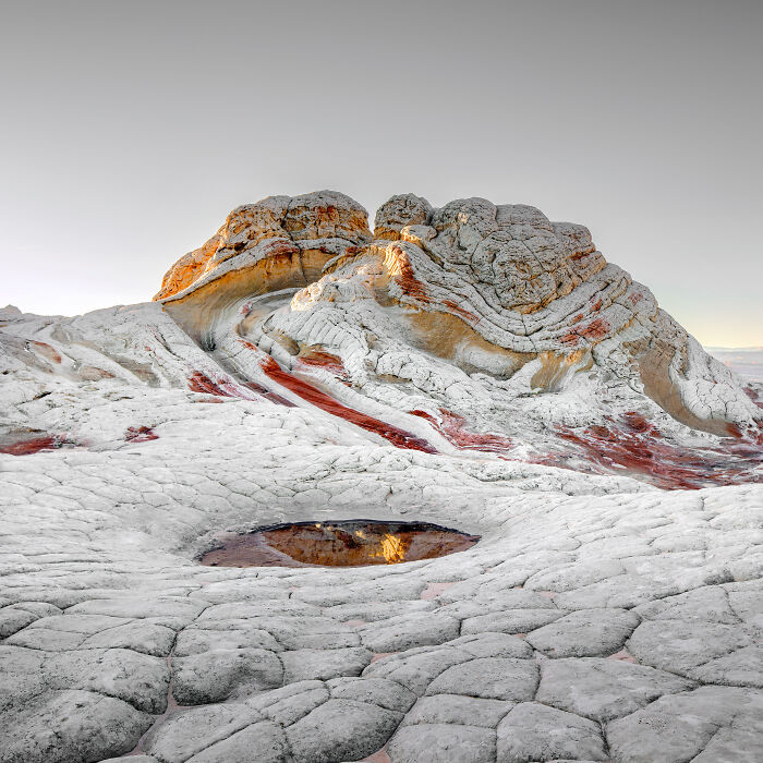 Stunning IPA 2024 finalist photo of a textured rock formation with a small reflective water pool in the foreground.