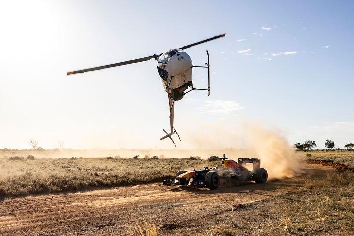Helicopter flying low over a race car on a dusty track, capturing a stunning photo moment from 2024 IPA winners and finalists.