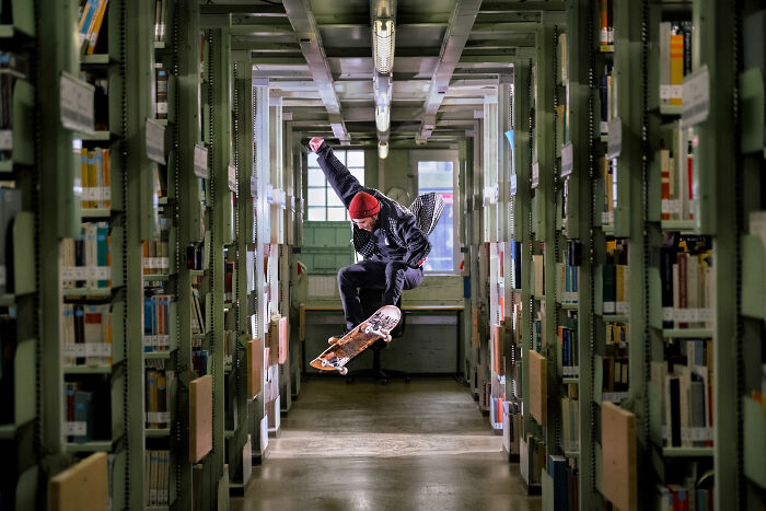 Skateboarder performing a trick in a library aisle, a stunning shot from the 2024 IPA winners collection.