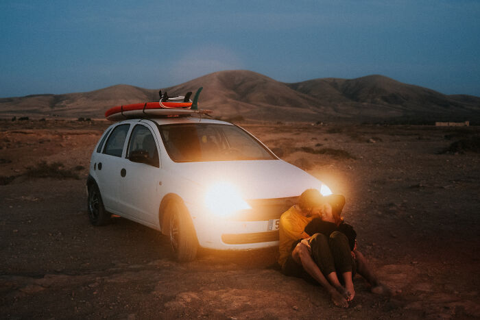 A couple sitting by a parked car with surfboards, enjoying a romantic moment in one of the best engagement photos of 2025.