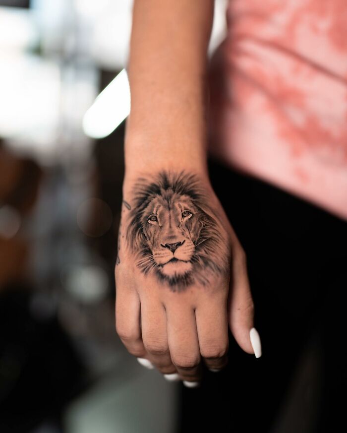 A realistic lion tattoo on a hand, showcasing tattoo art by Tatu Panda.