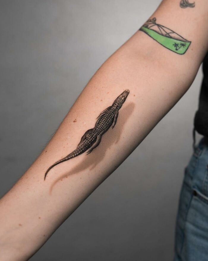Lifelike tattoo of a crocodile on an arm, designed by Tatu Panda, appearing three-dimensional.