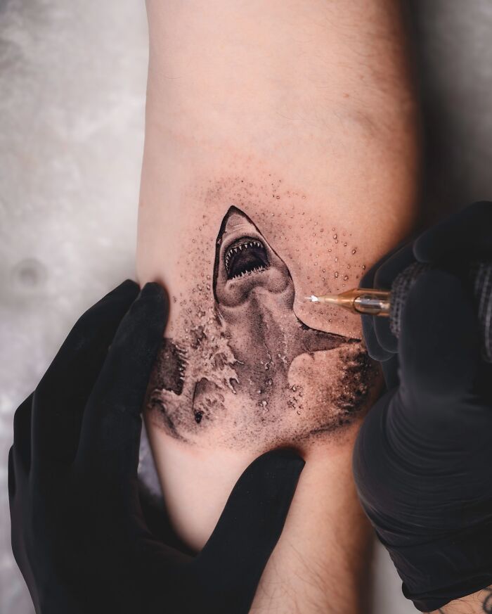 Tattoo artist Tatu Panda creating a lifelike shark tattoo on forearm, showcasing realistic aquatic design.