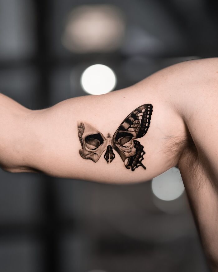 Lifelike tattoo by Tatu Panda on an upper arm, featuring a butterfly with a skull design blending into the wings.