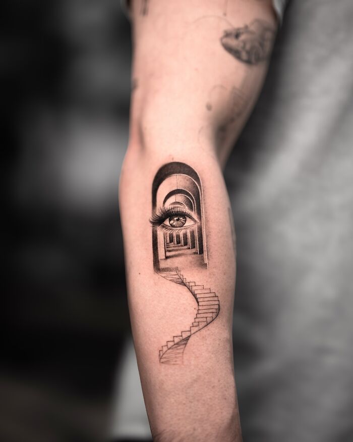 Lifelike tattoo by Tatu Panda depicting an eye in an archway with a winding staircase on an arm.