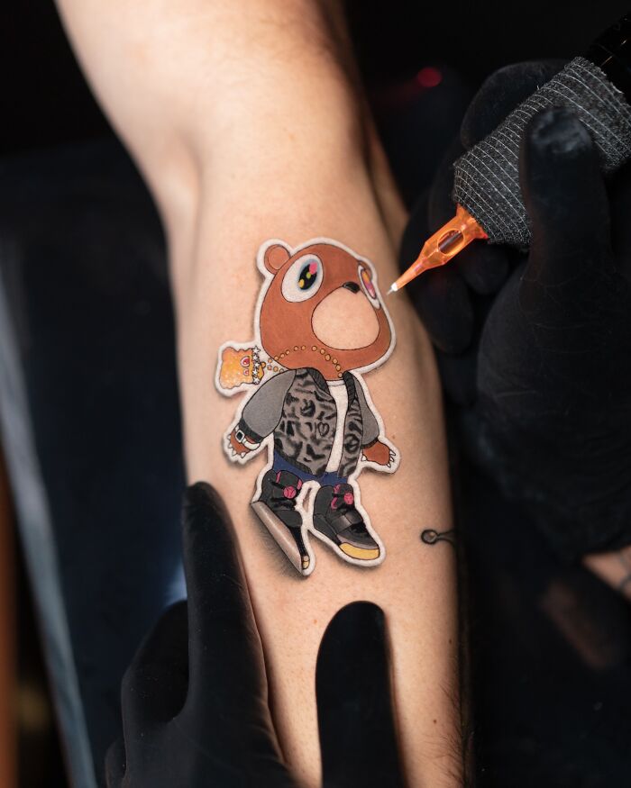 Tattoo artist creating a lifelike bear character tattoo on a person's arm, showcasing intricate details.