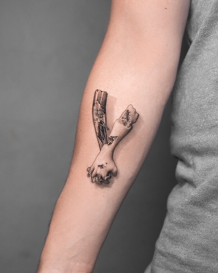 Lifelike tattoo by Tatu Panda depicting detailed hands clasping on a person's forearm.