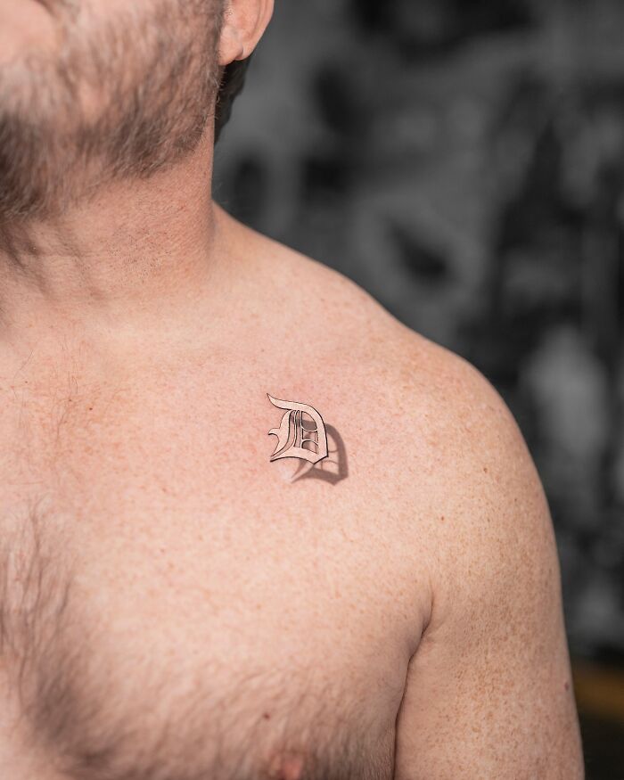 Lifelike tattoo of a stylized letter "D" on a person's chest by Tatu Panda.