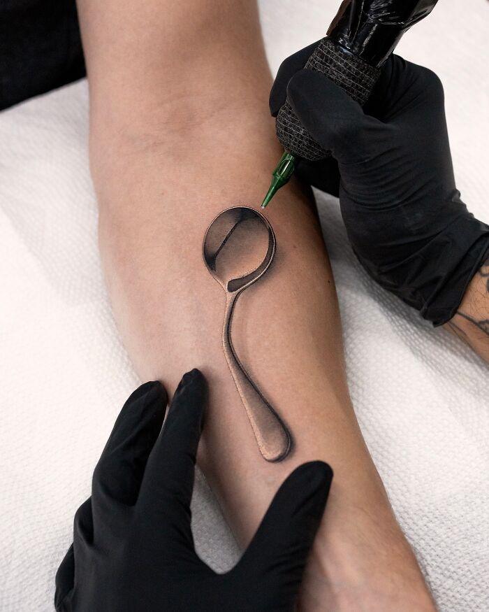 Tattoo artist Tatu Panda inking a lifelike spoon tattoo on an arm, showcasing realism and detail.