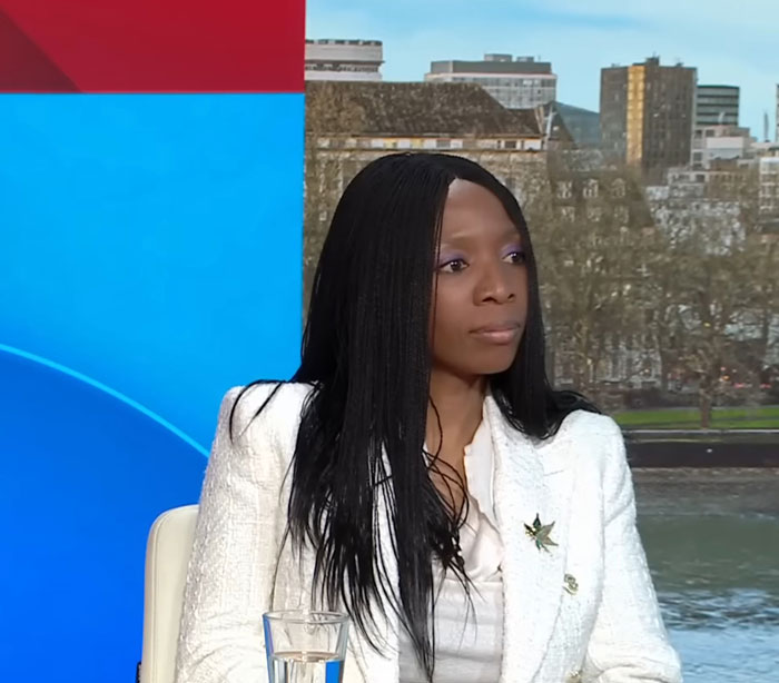 A woman in a white jacket on a TV set discussing Harry's charity and Meghan.