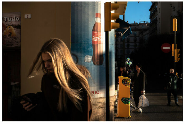 Street scene with people in shadow, featuring a bright Coca-Cola ad under the evening light.