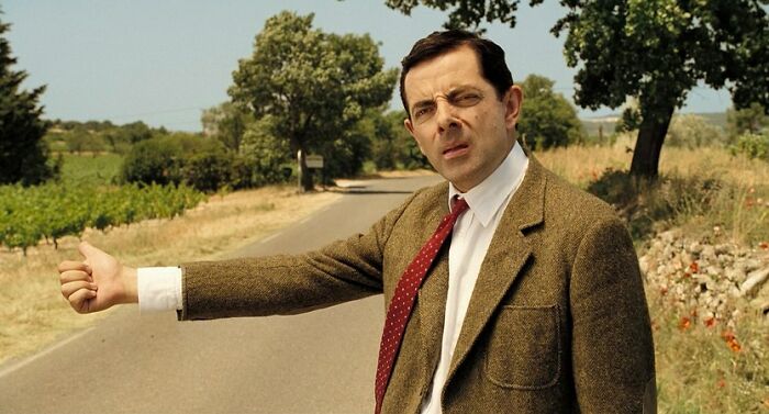 Man in a brown suit and red tie, hitchhiking on a rural road, showcasing actor's iconic role abilities.