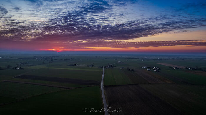 Aerial view of a city at sunset, showcasing fields, roads, and a vibrant sky.