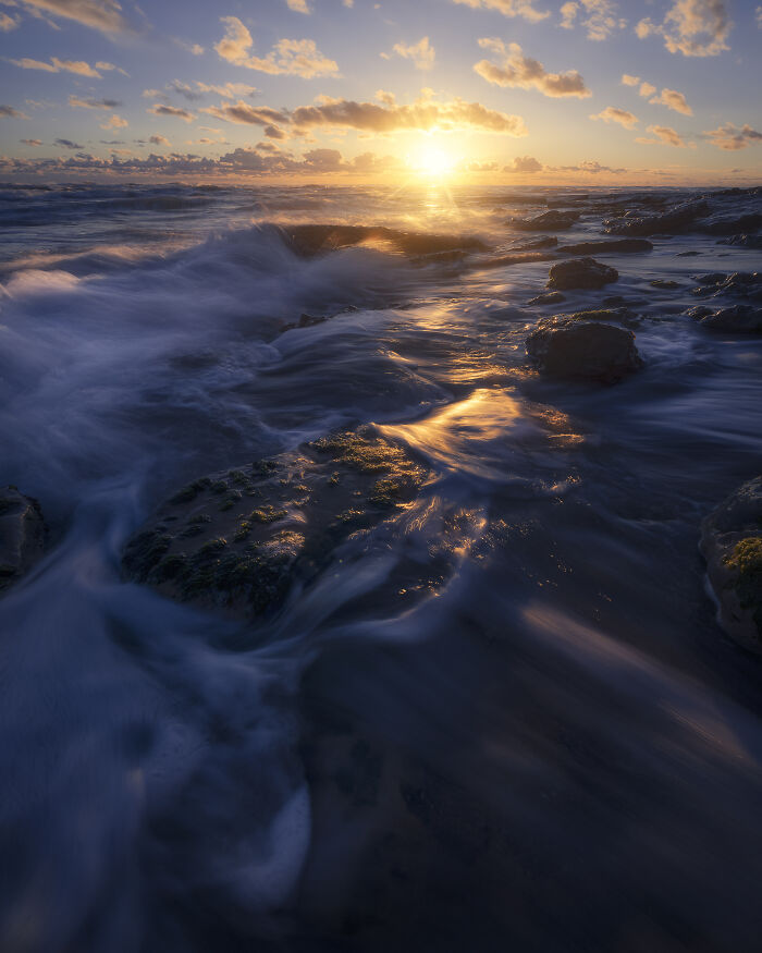 Stunning landscape of a sunset over ocean rocks, capturing serene waves and golden light.