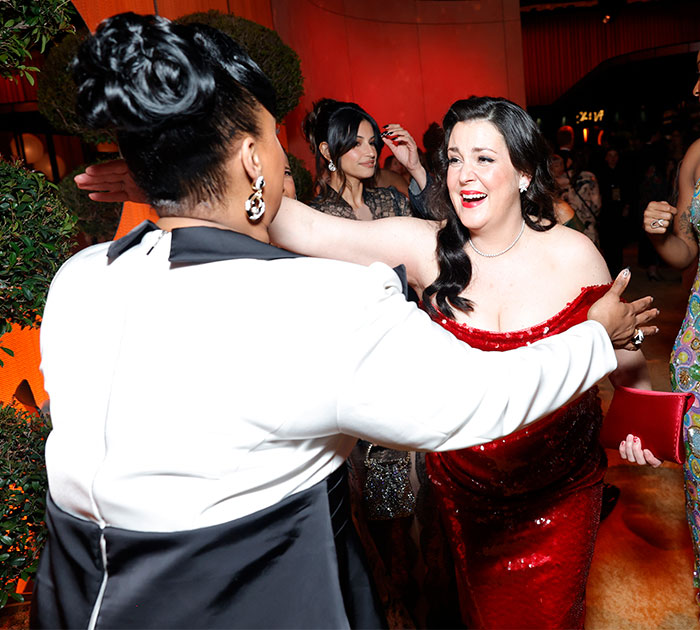 Two women joyfully hugging at Oscars 2025, one in a red dress, capturing behind the scenes moments unnoticed by many.