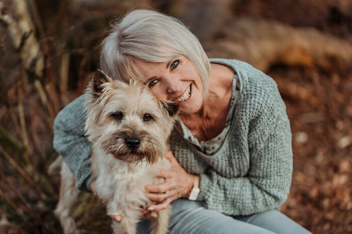 Senior woman joyfully hugging her small dog, showcasing a special bond between animals and their humans in a natural setting.