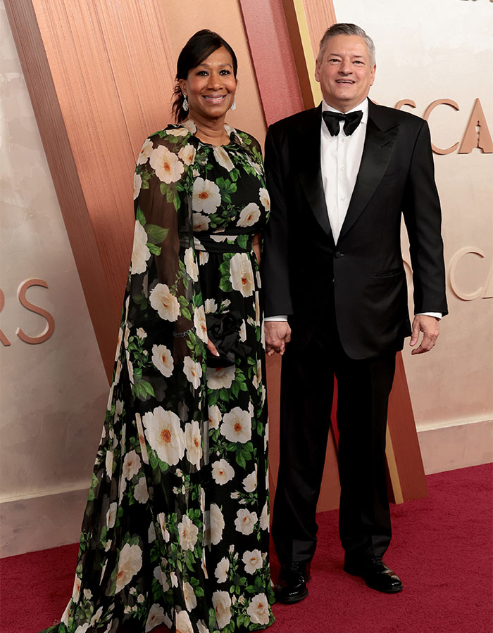 A couple on the Oscars 2025 red carpet, with fashionably challenged outfits in floral dress and classic tuxedo.