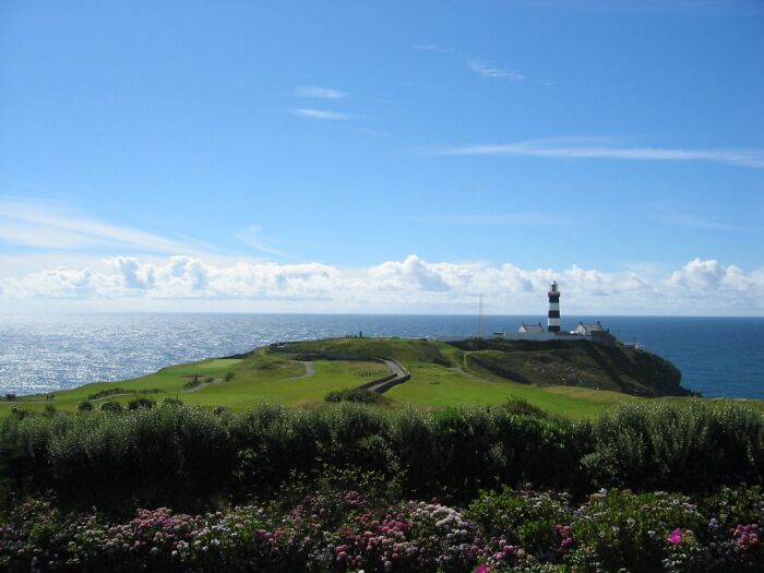 Breathtaking golf course by the sea with a lighthouse in the distance, offering panoramic ocean views.
