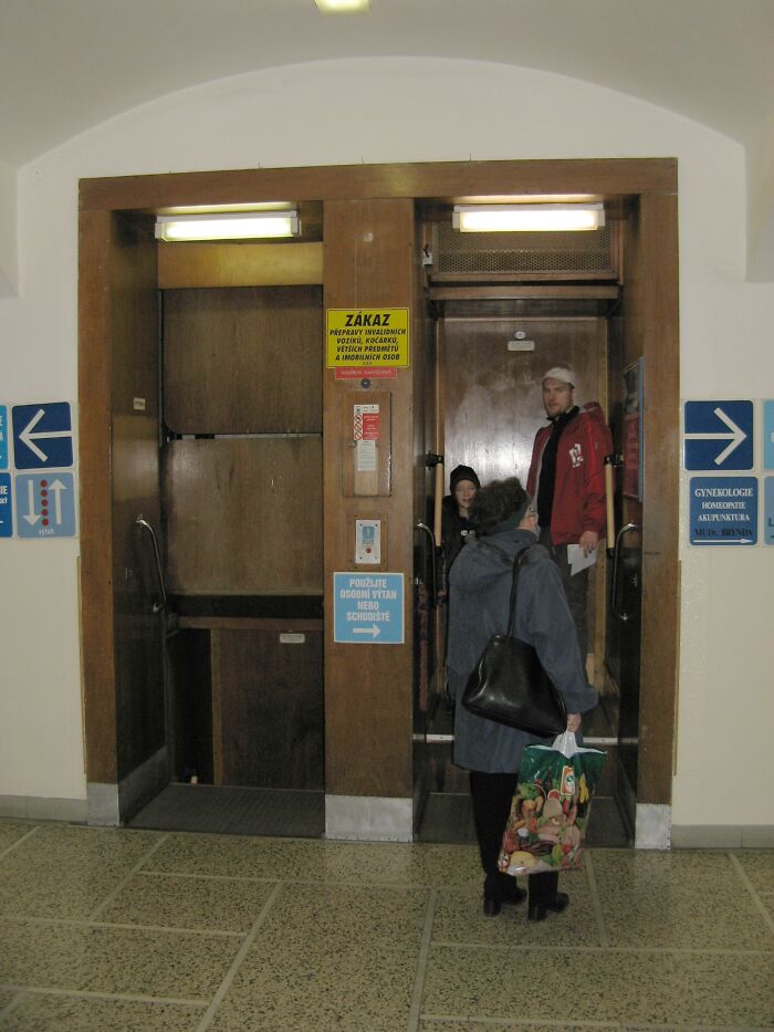 Paternoster lift, a weird invention, with passengers stepping on and off in a hallway setting.