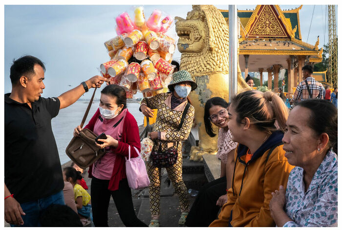 Street vendor sells snacks near a golden statue as people walk by, capturing a raw, unfiltered moment.
