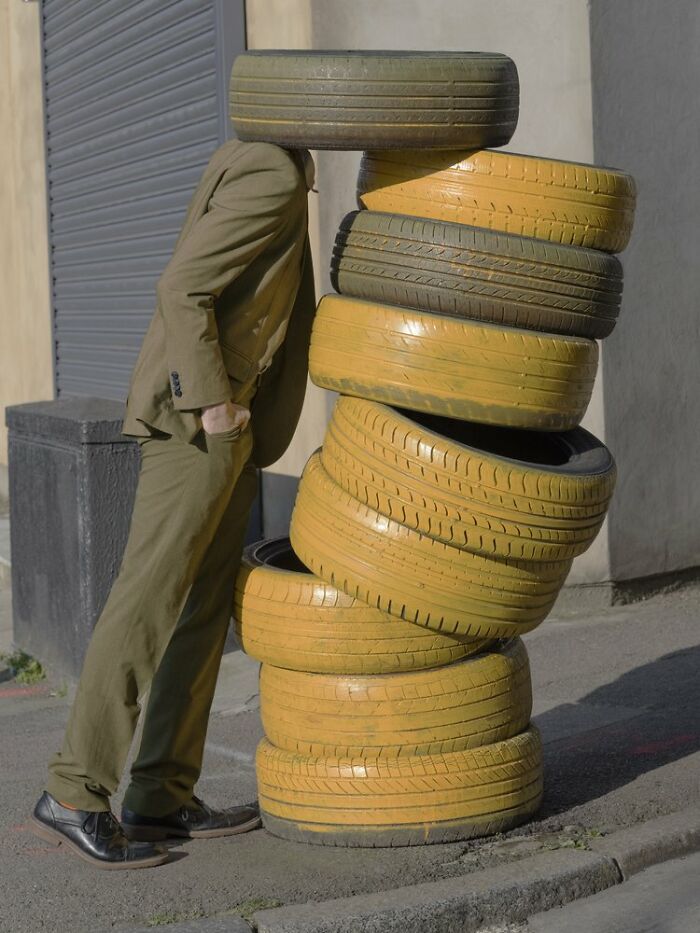 Surreal photograph by Ben Zank of a person in a suit standing with their head inside a stack of yellow tires.